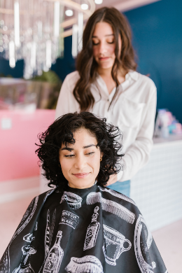 Hair stylist puts black cape on woman with black curly hair