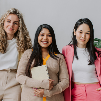 Three woman of different ethnicities stand together smiling