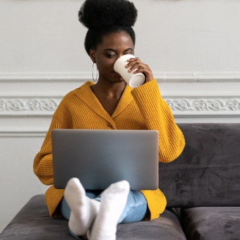 Woman sipping coffee on a couch looking at a laptop