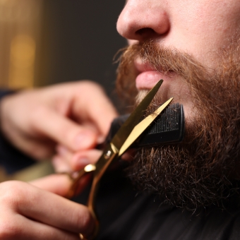 Cosmetologist trimming a beard with shears and a comb