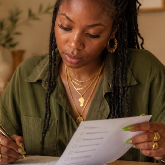 Young woman with braids wearing jewelry reviewing ducments holding a pen