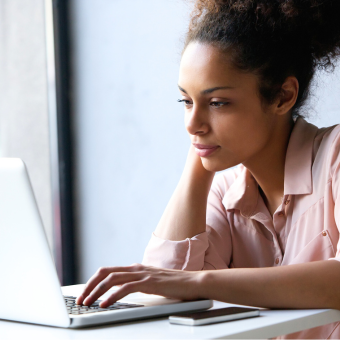 A woman looks intently at a laptop seated at a table