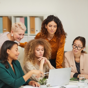 A group of professionals gathered around a laptop reviewing materials