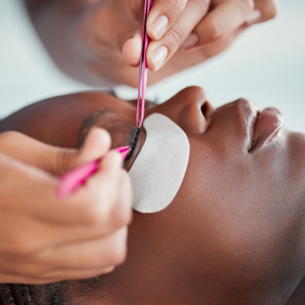 Model receiving eyelash extensions; eyelash extension tools hovering above her lashline