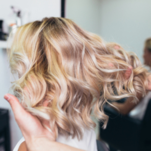 A woman sits in a hairdresser’s chair as her fresh balayage hairstyle is displayed