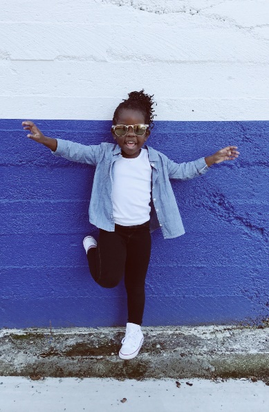 An image of young girl leaning on blue wall.