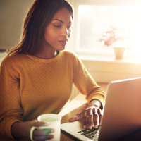 A stock image of female using laptop holding coffee cup
