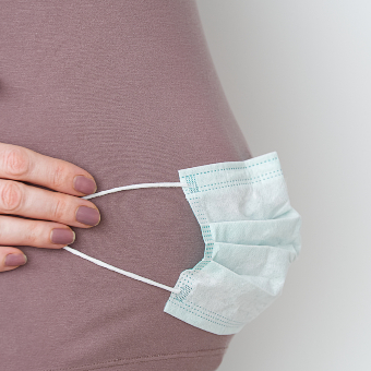 An image of pregnant woman with face mask on abdomen