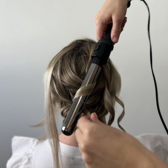 Using a curling iron to create curls over a bridal bun.