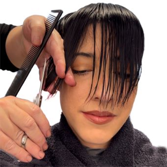 A hairstylist cuts their client’s bangs into a V shape.