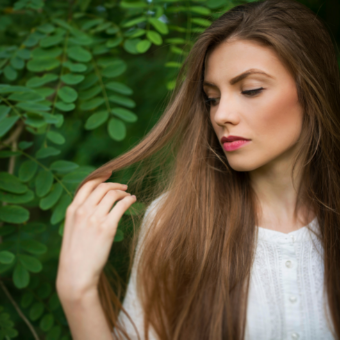 woman examines hair with trees in the background