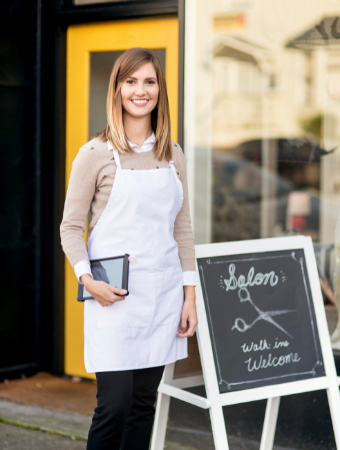 Hairdresser stands outside her salong with welcome sign