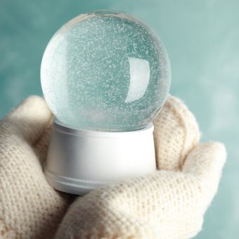 White mittens holding a snow globe against a teal background